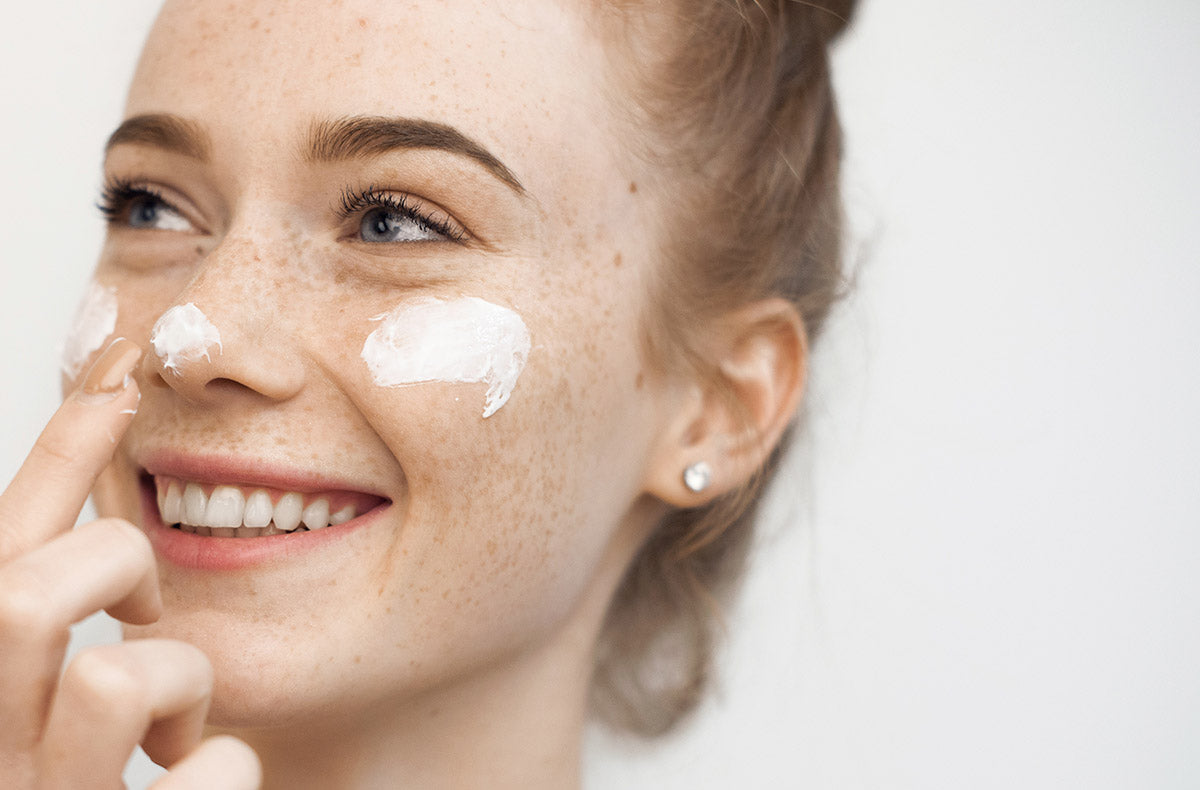 Smiling young woman applying cream to her face